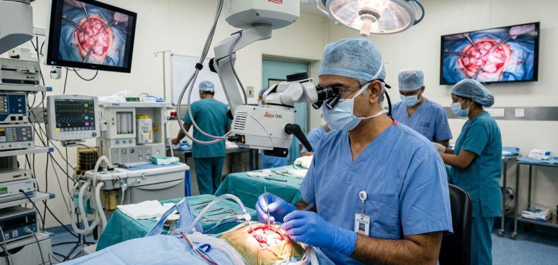 Dr. Ashok Kumar Indian neurosurgical team operating with high-power surgical microscope in modern operating theatre